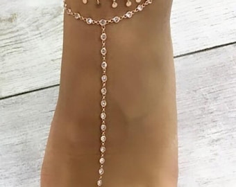 May include: A gold anklet with a turquoise beaded anklet and a shell charm. The anklet is layered with a delicate chain with small crystals.