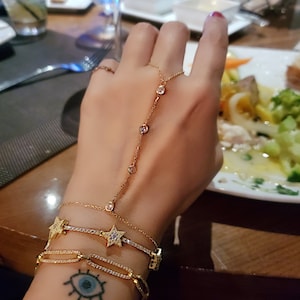 May include: A gold chain bracelet with a star charm and a ring with a clear stone. The bracelet is layered with a gold chain bracelet with a clear stone and a gold chain bracelet with a clear stone.