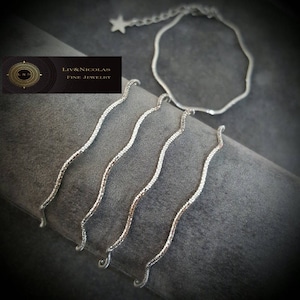 Op de afbeelding: Vijf zilveren kettingen met een golvend ontwerp. De kettingen zijn op elkaar gelegd en hangen aan een zilveren ketting met een stervormige hanger.