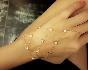 May include: A gold chain bracelet with small clear stones. The bracelet is designed to wrap around the wrist and up the hand, with a chain that extends to the finger.