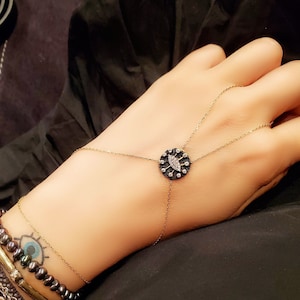 May include: A gold chain bracelet with a black and white evil eye charm. The charm is round and has a detailed design.