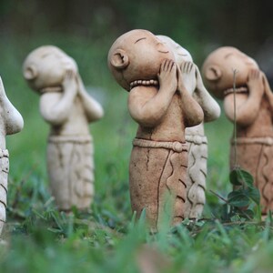 May include: A group of small, hand-painted ceramic figurines of people with their hands clasped in front of their faces. The figurines are arranged in a row on a bed of green grass.