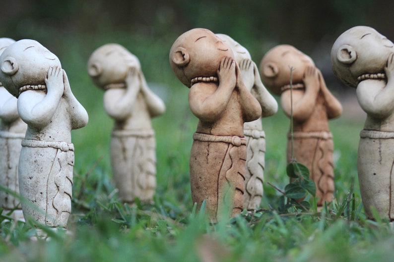 May include: A group of small, hand-painted ceramic figurines of people with their hands clasped in front of their faces. The figurines are arranged in a row on a bed of green grass.