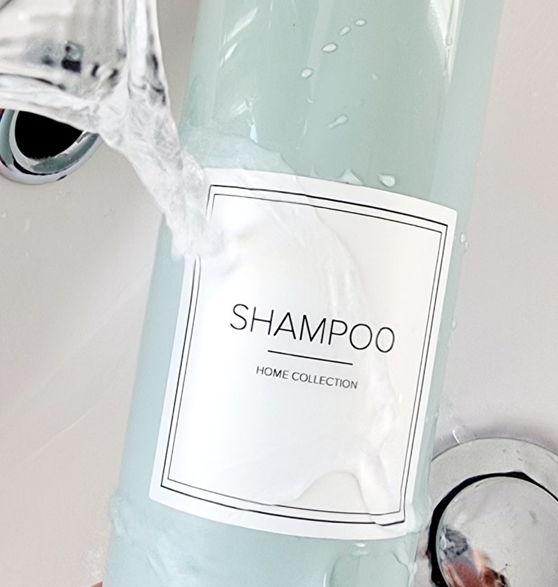 sage green pump dispenser bottle held under running tap to show white shampoo label applied as waterproof, label is cream with SHAMPOO written central in square label with thin line boarder around edge with HOME COLLECTION written smaller underneath