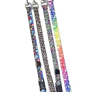 May include: A collection of four dog leashes with silver-colored metal clasps. The leashes feature various patterns, including floral, leopard print, and paw prints in vibrant colors. Each leash has a black plastic buckle.