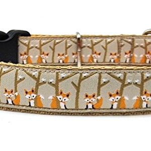 May include: A beige dog collar with a repeating pattern of orange foxes in a forest setting. The collar has a black buckle and a bright orange lining.