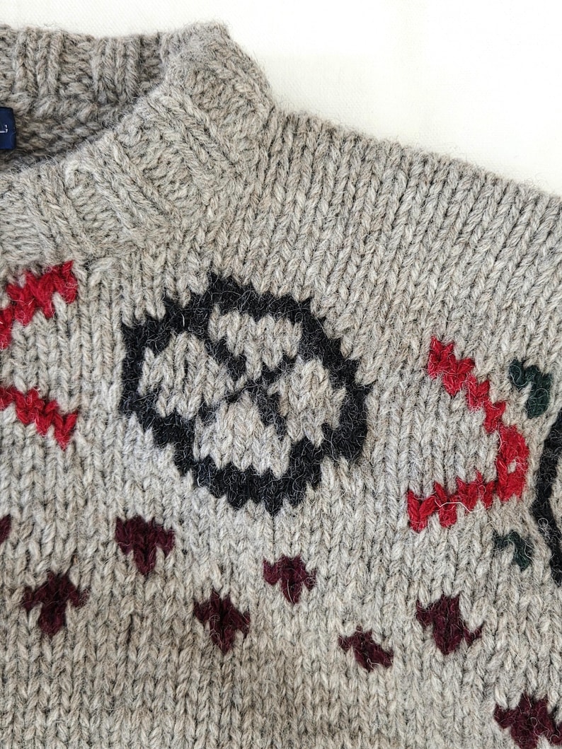 Peut inclure: Gros plan sur un pull en tricot gris avec un col montant. Le pull pr&eacute;sente un motif g&eacute;om&eacute;trique noir et rouge, ainsi que des accents bordeaux et verts. Le tricot est fait d'un fil &eacute;pais et textur&eacute;.