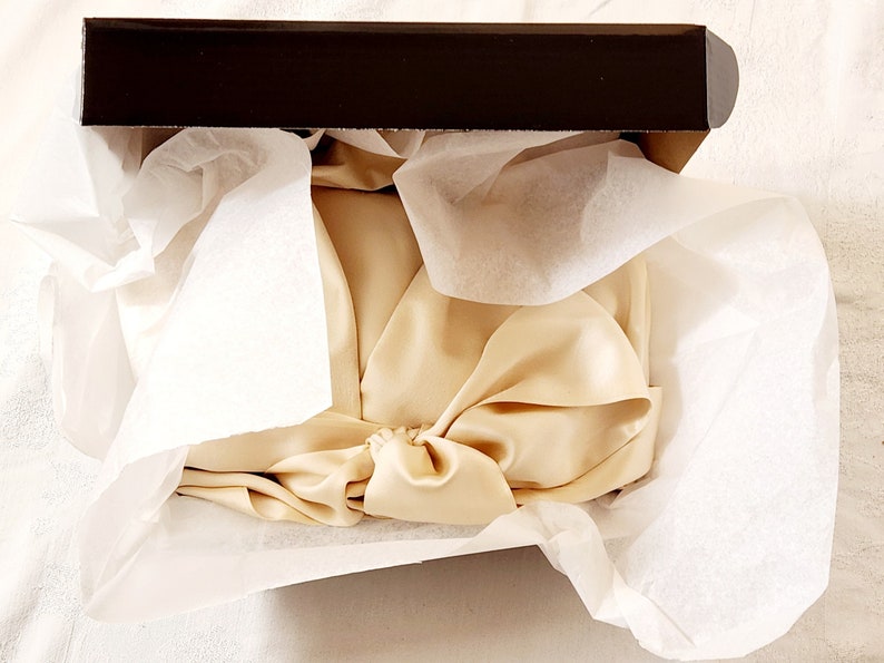 May include: A beige silk scarf is folded and placed inside a brown gift box lined with white tissue paper.