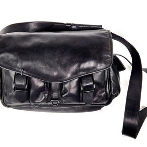 May include: A black leather messenger bag with multiple pockets and a long adjustable strap.