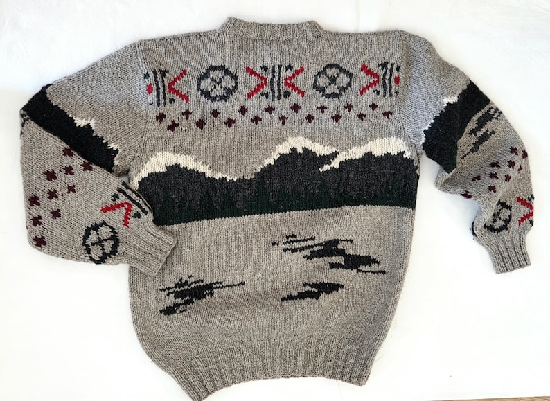 Peut inclure: Pull en tricot gris avec un motif de montagne et g&eacute;om&eacute;trique. Le pull pr&eacute;sente des accents noirs, blancs et rouges. Les manches ont des rayures noires et des motifs g&eacute;om&eacute;triques rouges et noirs. Un v&ecirc;tement confortable, chaud et &eacute;l&eacute;gant.