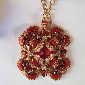 Könnte beinhalten: Eine rote und goldene Perlenkette mit einem großen roten Edelstein in der Mitte. Der Anhänger hat die Form eines Sternbursts.