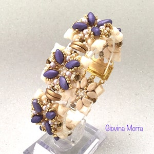 Peut inclure: Un bracelet en perles de couleur pourpre et blanche avec un fermoir doré. Le bracelet présente un motif floral avec plusieurs couches de perles.