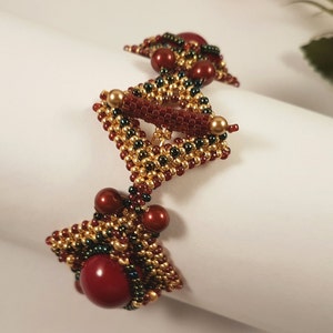 Peut inclure: Un bracelet en perles avec un motif g&eacute;om&eacute;trique dans les tons or, vert et rouge. Le bracelet pr&eacute;sente une forme triangulaire centrale avec des triangles plus petits de chaque c&ocirc;t&eacute;.