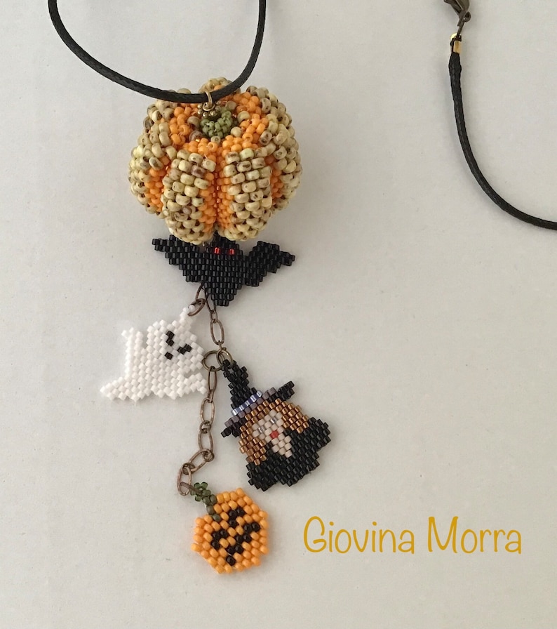 May include: A beaded necklace with a pumpkin charm, a bat charm, a ghost charm, a witch charm, and a small pumpkin charm. The necklace is made of black cord and has a gold chain connecting the charms. The charms are all made of beads and are in various colors, including orange, black, white, and green. The necklace is signed "Giovina Morra".
