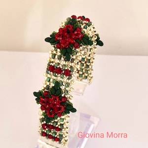 May include: A beaded bracelet with red and green flowers. The bracelet is made with small seed beads and features a gold metallic thread.