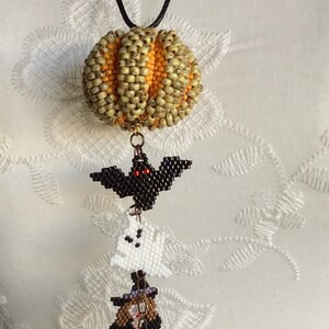 May include: A beaded Halloween necklace with a pumpkin, bat, ghost, witch, and a smaller pumpkin charm. The necklace is made of black cord and has a gold chain connecting the charms.