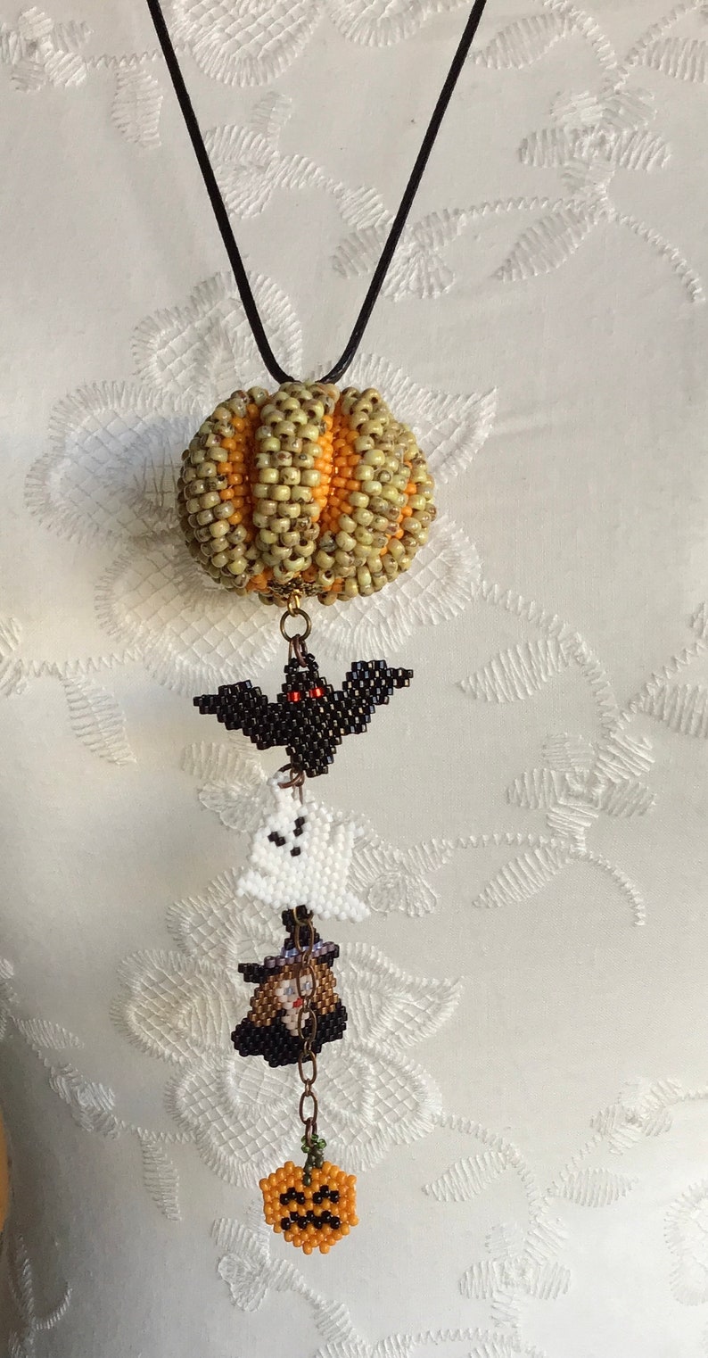May include: A beaded Halloween necklace with a pumpkin, bat, ghost, witch, and a smaller pumpkin charm. The necklace is made of black cord and has a gold chain connecting the charms.