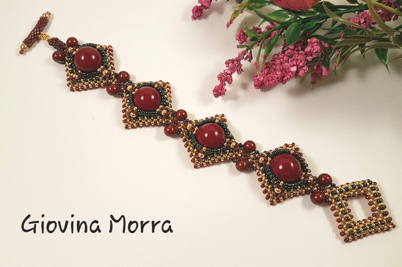 Peut inclure: Un bracelet en perles avec un motif g&eacute;om&eacute;trique compos&eacute; de perles rouges, dor&eacute;es et vertes. Le bracelet a un fermoir carr&eacute; et est orn&eacute; de perles de pierres pr&eacute;cieuses rouges.