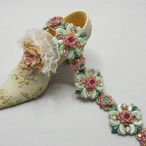 Può includere: Una scarpa in ceramica bianca con un motivo floreale e una ghirlanda di fiori perlati con accenti rosa e verdi.