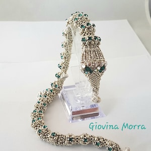 Può includere: Un braccialetto di perline argentate e verdi con un design a nappina. Il braccialetto è realizzato con piccole perline rotonde e presenta un gruppo di perline verde smeraldo nella parte superiore della nappina.