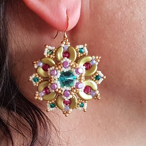 以下が含まれることがあります： 緑、紫、赤のビーズで花柄のデザインが施されたゴールドのイヤリング。花の真ん中には大きなターコイズ色の宝石が埋め込まれています。