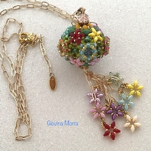 May include: A gold-tone necklace featuring a beaded pendant with a floral design in various colors, including red, yellow, and blue. The pendant is spherical with a tassel of small flower charms. The necklace has a delicate chain and a lobster clasp.