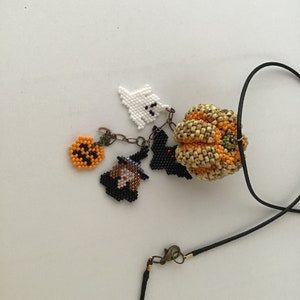 May include: A black beaded necklace with a variety of Halloween-themed charms, including a pumpkin, a ghost, a witch, and a bat.