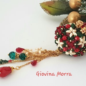 May include: A Christmas-themed beaded necklace featuring a red, white and green ornament. The ornament is a sphere with a snowflake design. The necklace has a gold chain and red and green beads.