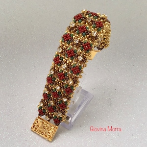 May include: A detailed beaded bracelet with a gold clasp. The bracelet showcases a pattern of red and green floral designs, accented with clear crystals, set against a gold backdrop. The clasp is rectangular.