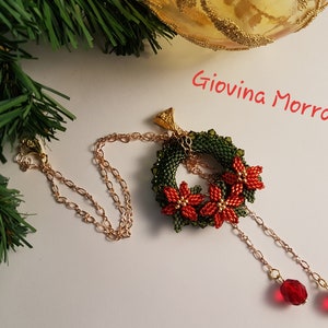 May include: A gold chain necklace with a beaded Christmas wreath pendant featuring red poinsettia flowers and green leaves. The necklace has two dangling red crystal beads.