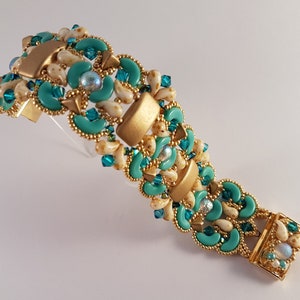 Könnte beinhalten: Ein goldenes und türkisfarbenes Armband mit einem Verschluss. Das Armband ist aus kleinen, runden Perlen gefertigt und hat ein geometrisches Design.