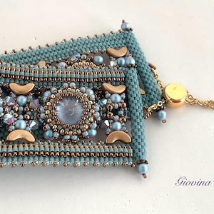 Könnte beinhalten: Ein blaues und goldenes Perlenarmband mit einem dekorativen Verschluss. Das Armband hat ein geometrisches Design mit mehreren Perlenreihen und einem zentralen Blickfang.