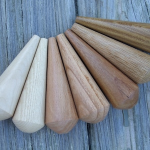 May include: A collection of seven wooden furniture legs, each with a conical shape and rounded base. The legs vary in color from light beige to dark brown, showcasing the natural wood grain. They are arranged in a fan-like pattern.