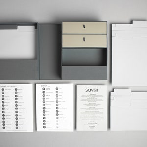 May include: A gray box with two drawers and a compartment for storing recipe cards. The box is open and the drawers are pulled out. There are several sheets of paper with recipe categories and a welcome letter from the company "savor".