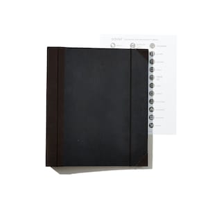 May include: A black, textured, expandable folder with brown edges. The folder has a tab on the right side with a list of categories for travel labels, including "Africa", "Beaches & Islands", "Monuments", "Nature", and more.