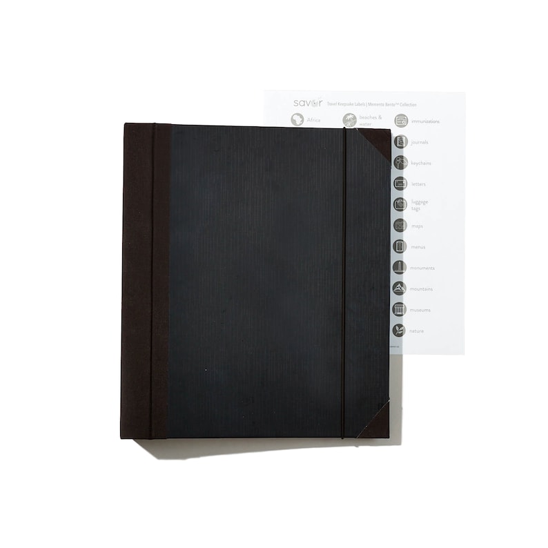 May include: A black, textured, expandable folder with brown edges. The folder has a tab on the right side with a list of categories for travel labels, including "Africa", "Beaches & Islands", "Monuments", "Nature", and more.