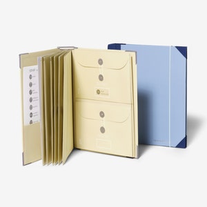 May include: A light blue folder with a white elastic band closure and a yellow folder with multiple envelopes and a list of numbers and titles. The text on the folder reads "Vacay Vibes".