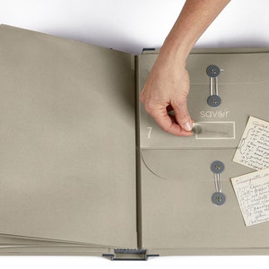 May include: A gray recipe binder with a clear plastic pocket labeled "savor" and a handwritten recipe card inside. The binder has a number "7" on the front and is open to reveal a clear plastic pocket on the right side.