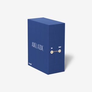 以下が含まれることがあります： 「THE VAULT」と「ADELAIDE」の文字が印刷された青い箱。箱には紐が結ばれており、2つのボタンが付いています。