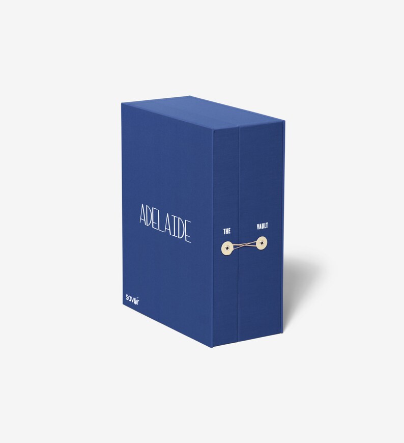 以下が含まれることがあります： 「THE VAULT」と「ADELAIDE」の文字が印刷された青い箱。箱には紐が結ばれており、2つのボタンが付いています。