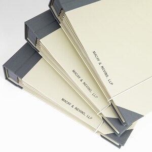 May include: Three gray and cream-colored legal binders with the text "MACAY & NEVINS, LLP" printed on the front.