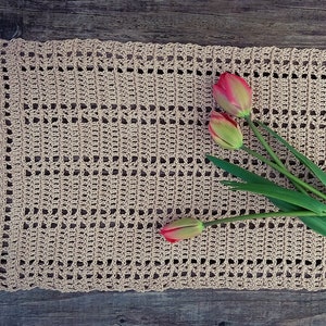 May include: A beige crocheted table runner with three red and yellow tulips on top.