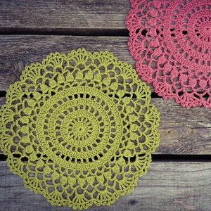 May include: Two crocheted doilies, one green and one pink, on a wooden surface.