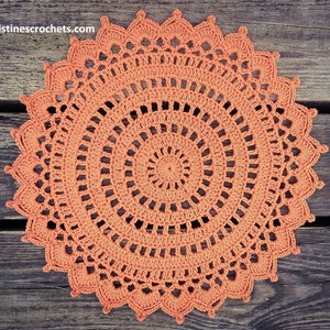 May include: A large, round, crocheted doily in a bright orange colour. The doily has a delicate, intricate design with multiple layers of crocheted circles.