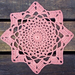 May include: A pink crocheted doily with a starburst design. The doily is made with a delicate, lacy pattern and has a circular center.