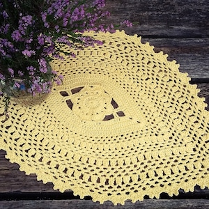 Puede incluir: Un encaje de ganchillo amarillo con un delicado patrón floral. El encaje está colocado sobre una superficie de madera.