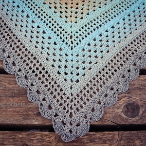 May include: A crocheted shawl with a gradient of blue, teal, and gray colors. The shawl has a scalloped edge and is made with a delicate stitch pattern.