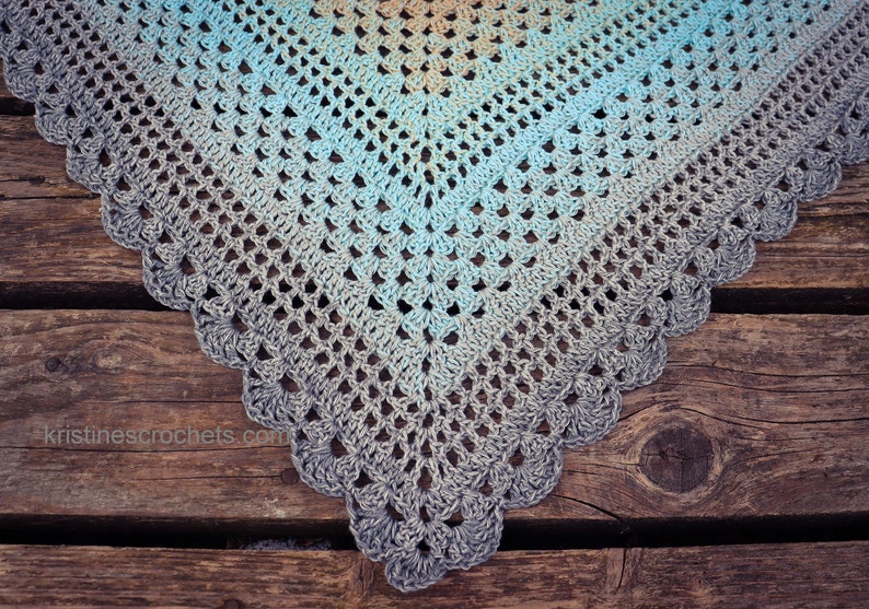May include: A crocheted shawl with a gradient of blue, teal, and gray colors. The shawl has a scalloped edge and is made with a delicate stitch pattern.