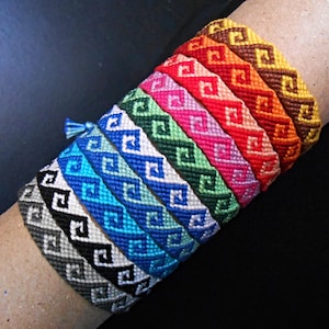 May include: A collection of colorful friendship bracelets. Each bracelet features a geometric pattern in various colors, including blue, green, pink, red, orange, and yellow. The bracelets are displayed on a brown cylindrical object.