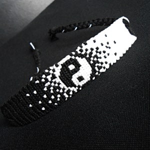 Peut inclure: Bracelet d'amitié noir et blanc fait à la main avec un symbole Yin Yang. Le bracelet est fait de fils tissés, avec un effet dégradé du noir au blanc. Le symbole Yin Yang est centré sur le bracelet.